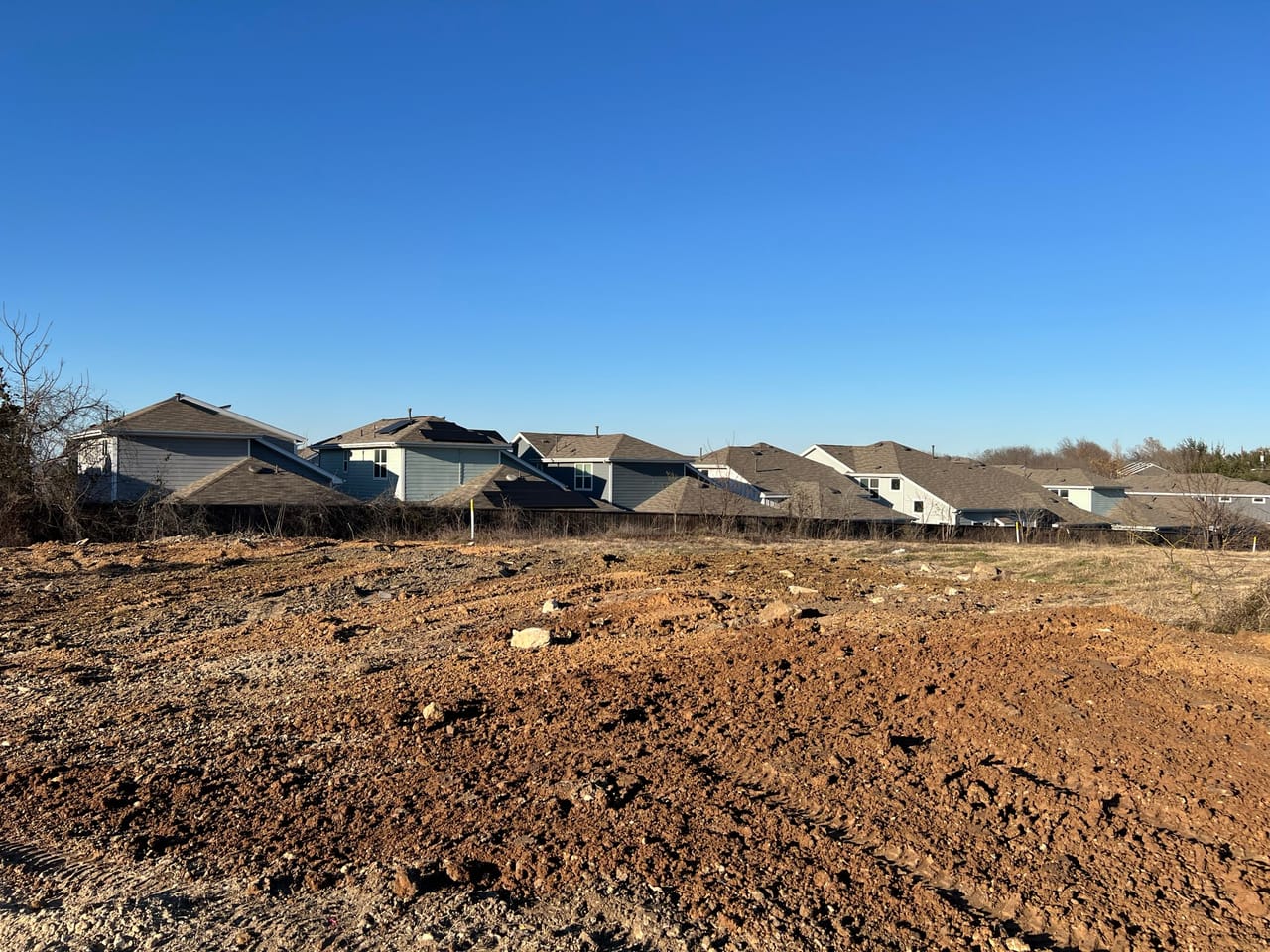 Wide graded dirt lot ready for construction with homes behind in Kyle, TX