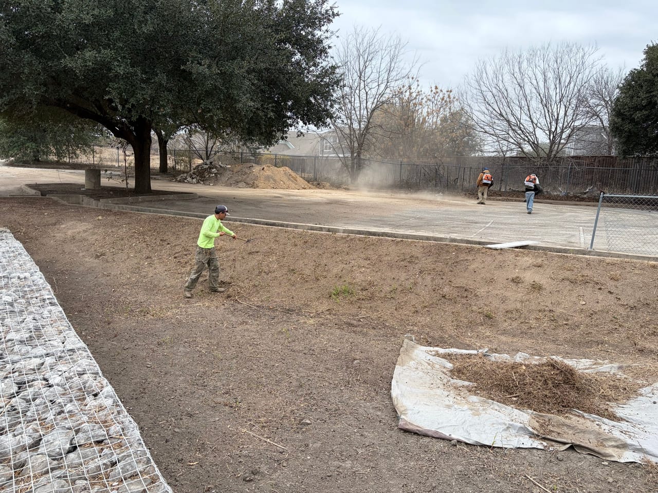 Worker spreading soil in a dusty detention basin with erosion fabric rolls in Central Texas
