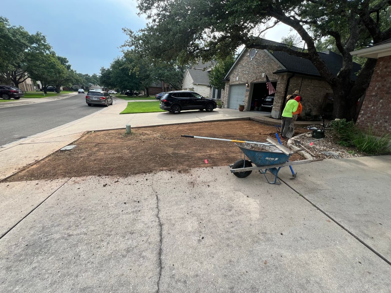 Worker with wheelbarrow smoothing graded soil beside a driveway in Bee Cave, TX