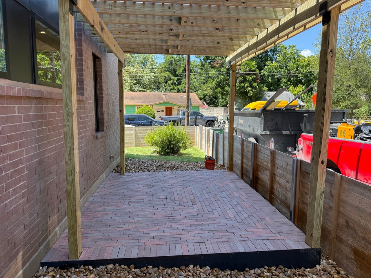 Brick paver walkway running under the pergola between fence and house by Corral Bros in Central Texas