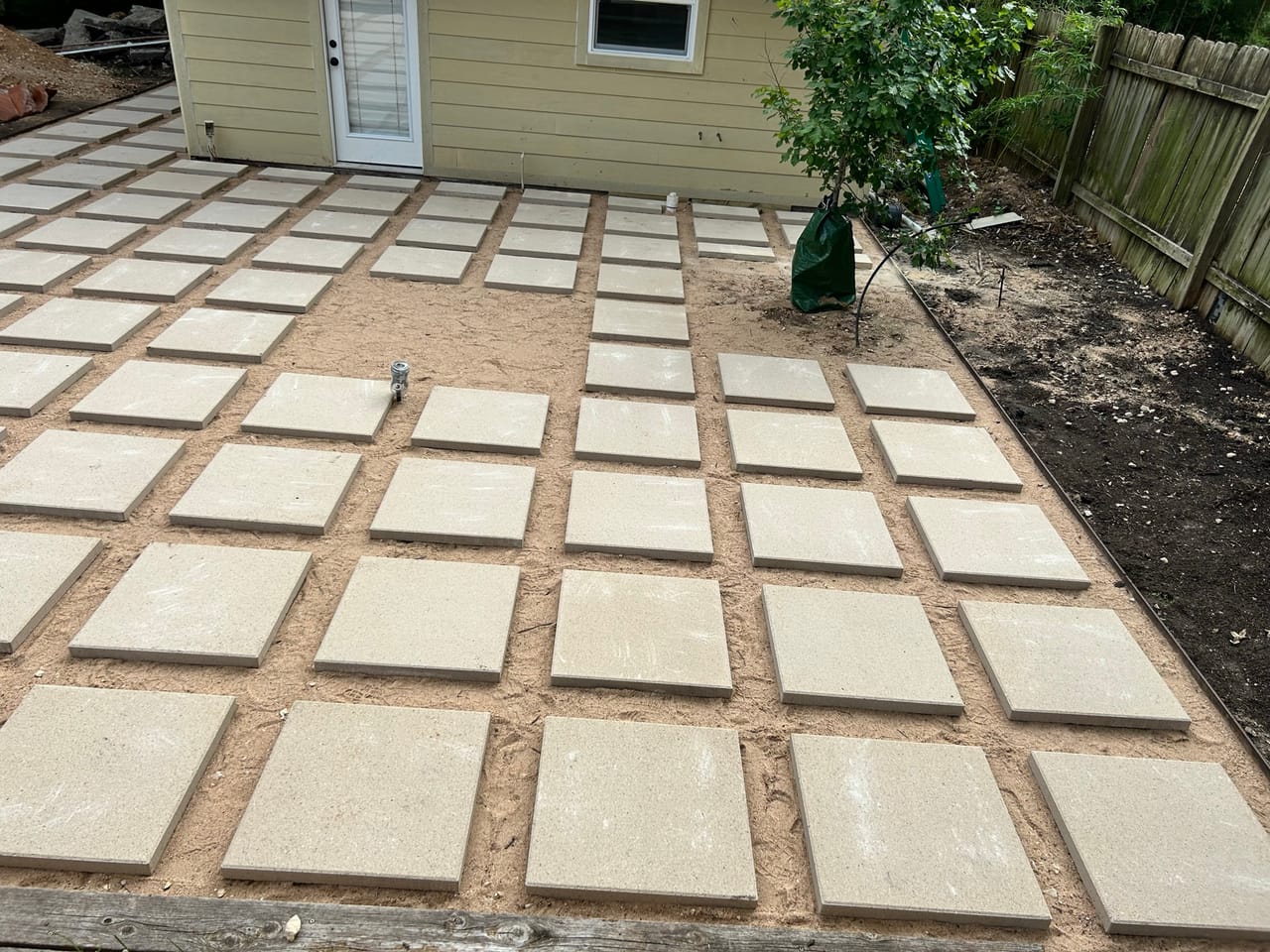 Finished concrete paver patio in grid pattern beside wood fence in San Antonio, TX