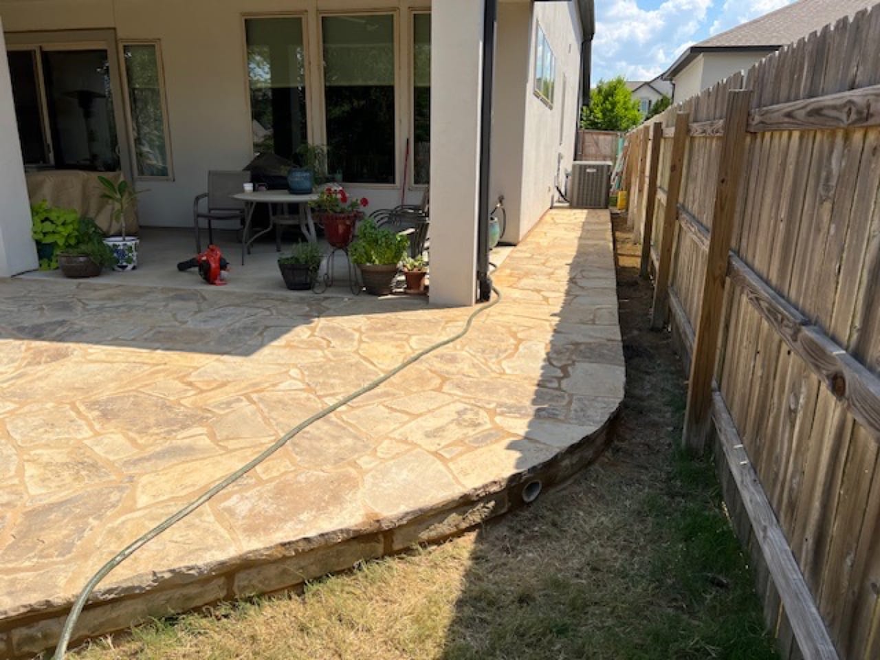 Finished flagstone patio curving toward the fence with hose coiled in Central Texas