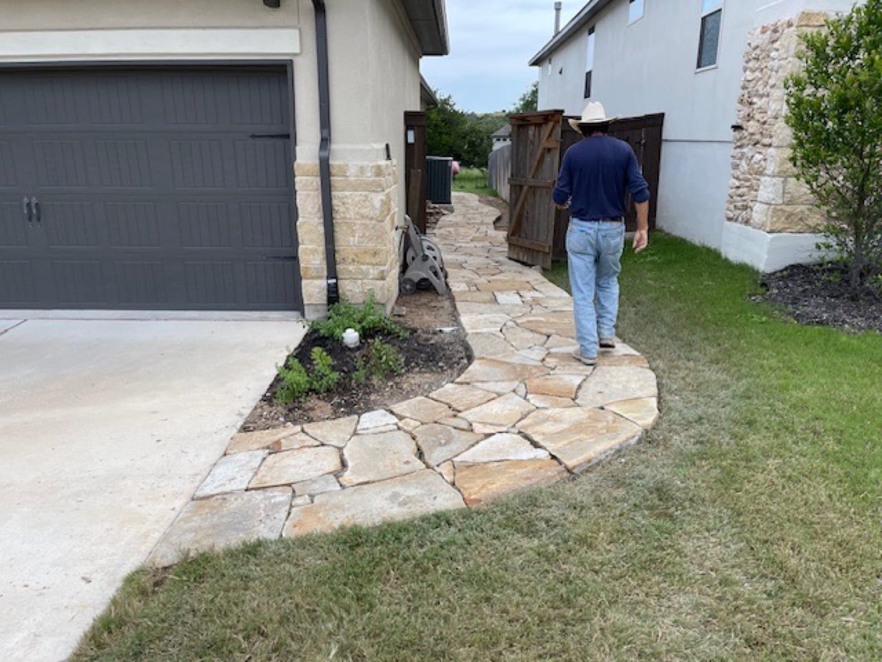 Finished flagstone walkway beside garage with man walking away in Lockhart, TX