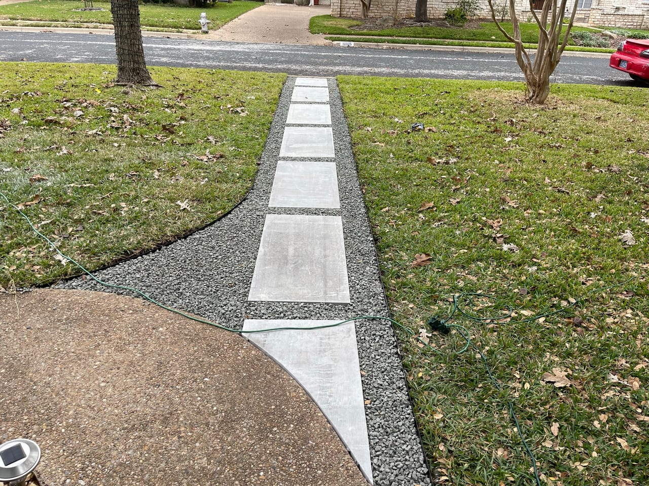 Finished paver and gravel walkway crossing a green front lawn in Schertz, TX