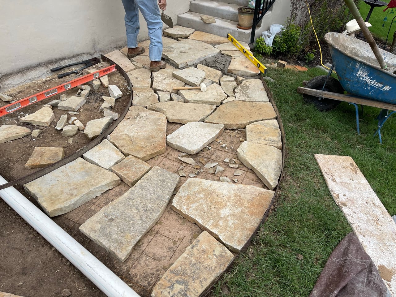 Flagstone patio being set in place with wheelbarrow and level nearby by Corral Bros in Central Texas