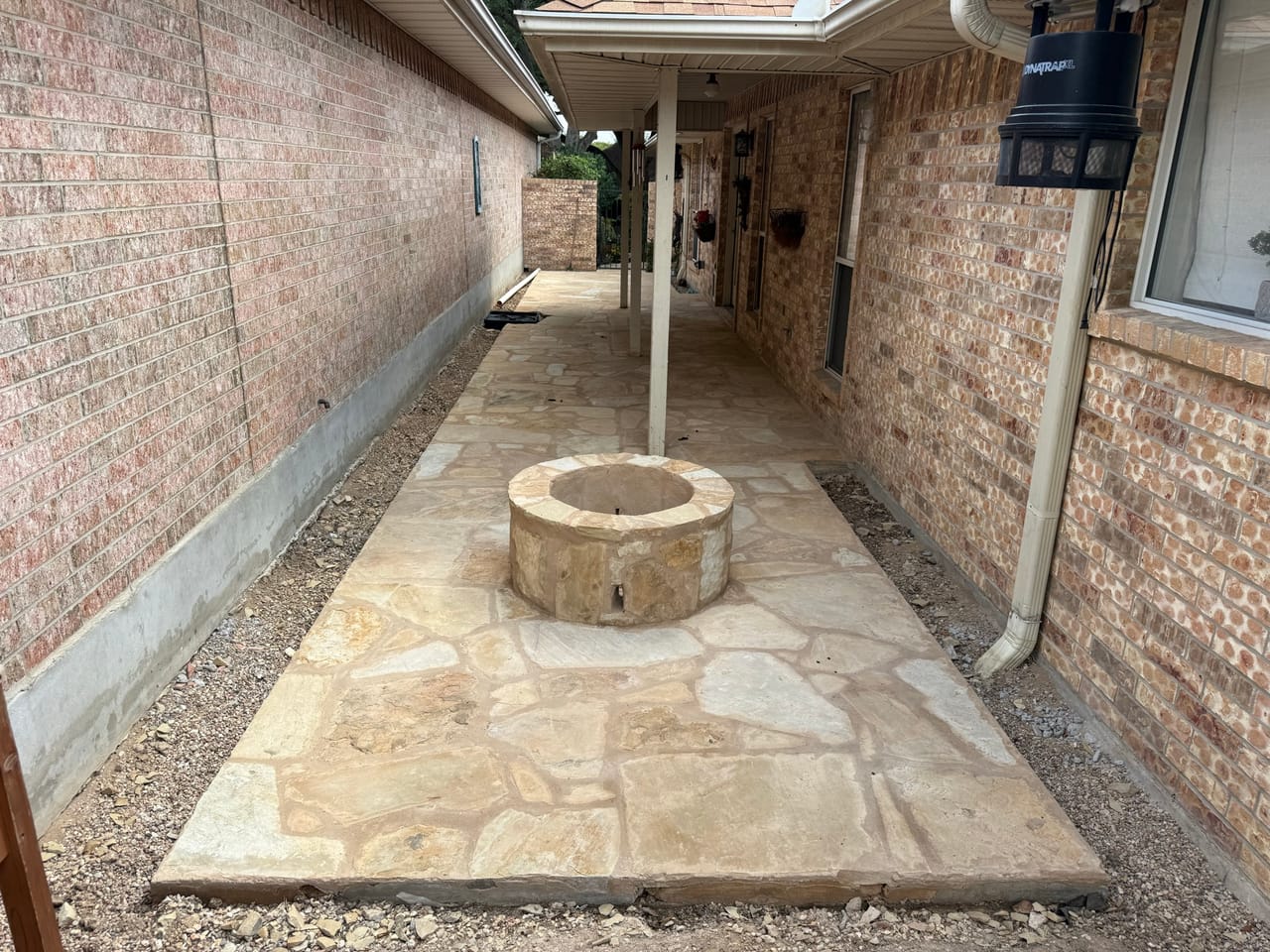 Flagstone side patio with round stone fire pit against brick house in Central Texas