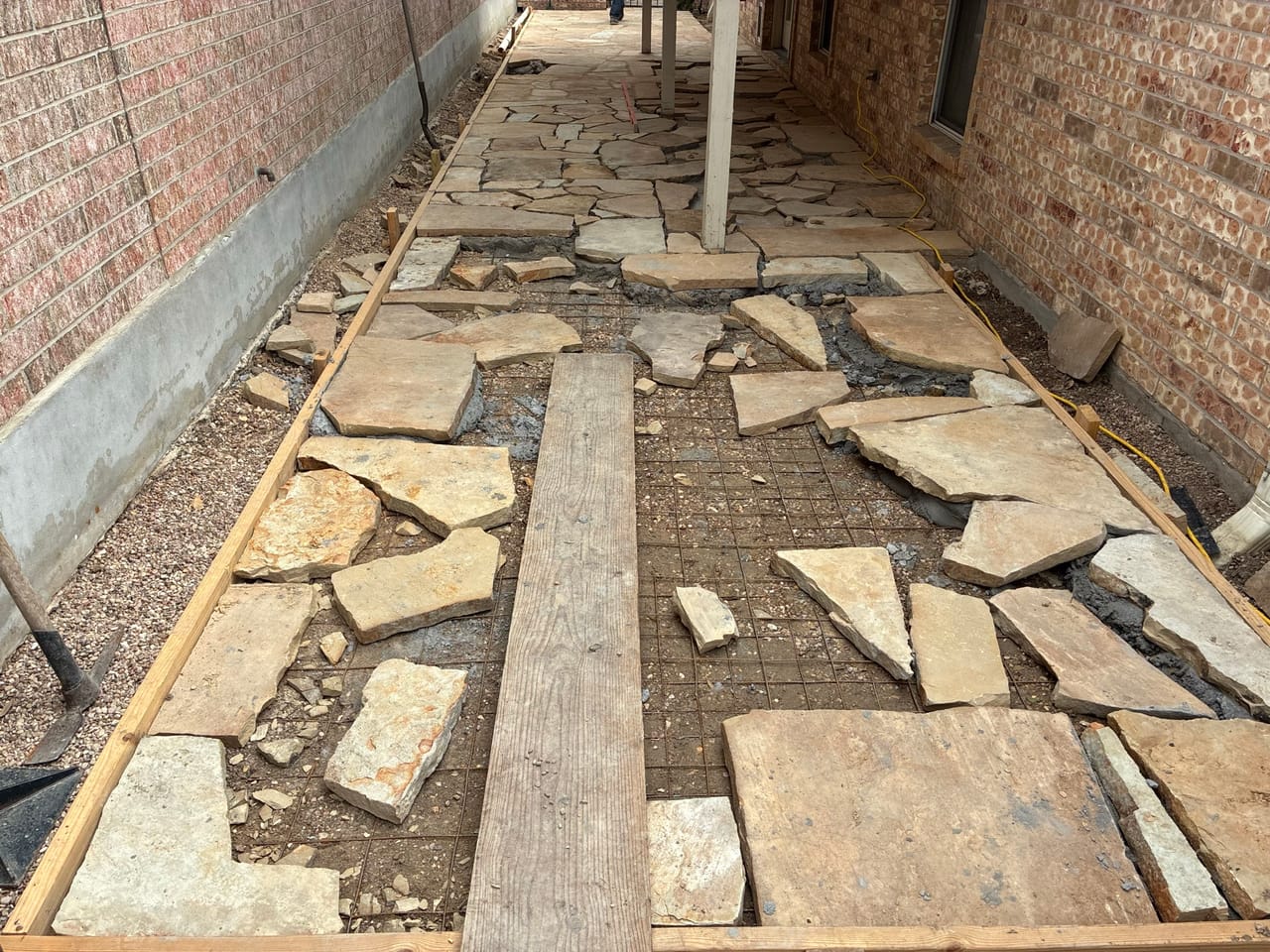 Flagstone walkway being laid along a brick house with stones unset by Corral Bros in Central Texas