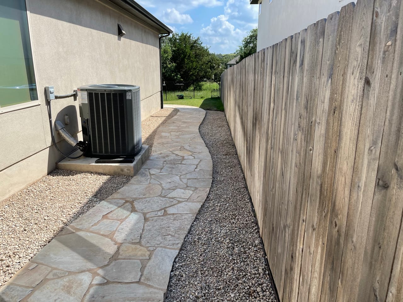 Flagstone walkway with gravel border passing an outdoor AC unit in Leander, TX