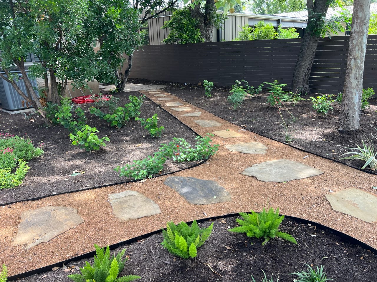 Flagstone walkway winding through mulch beds along a dark fence in Dripping Springs, TX