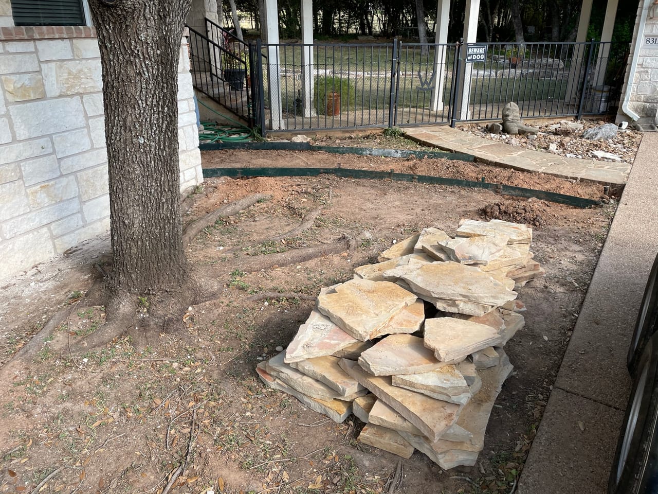 Stacked flagstone pallets on dirt beside a big shade tree by Corral Bros in Central Texas