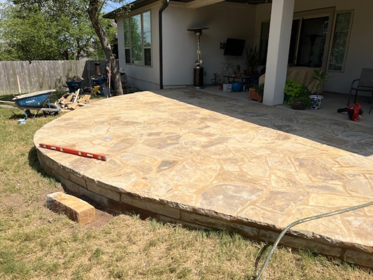 Sunlit finished flagstone patio with raised stone border and lawn in Central Texas