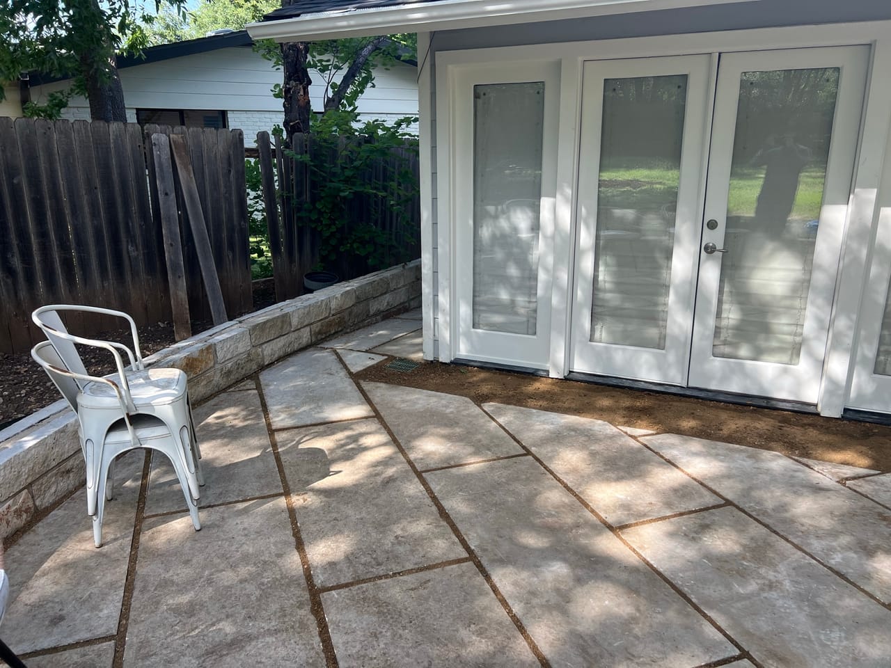 Wider view of the finished stone patio with a white metal chair in Central Texas
