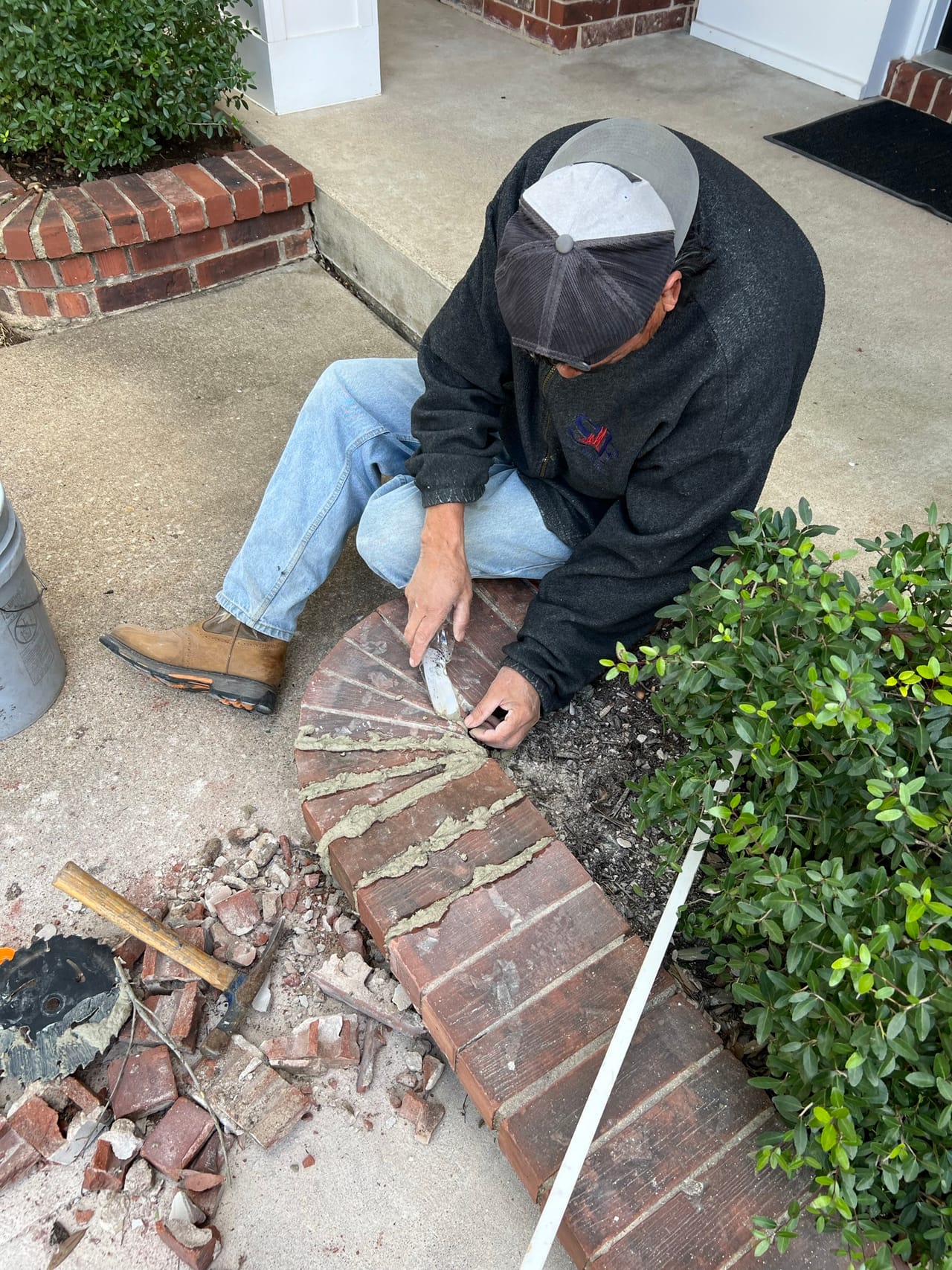 Worker kneeling to set brick edging beside shrubs and concrete by Corral Bros in Central Texas