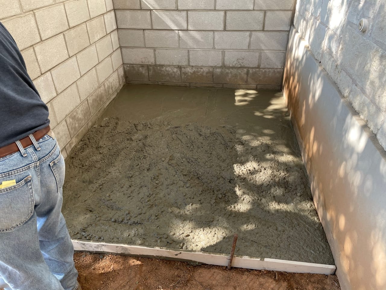 Worker screeding a sand base inside a new stone walled courtyard by Corral Bros in Central Texas