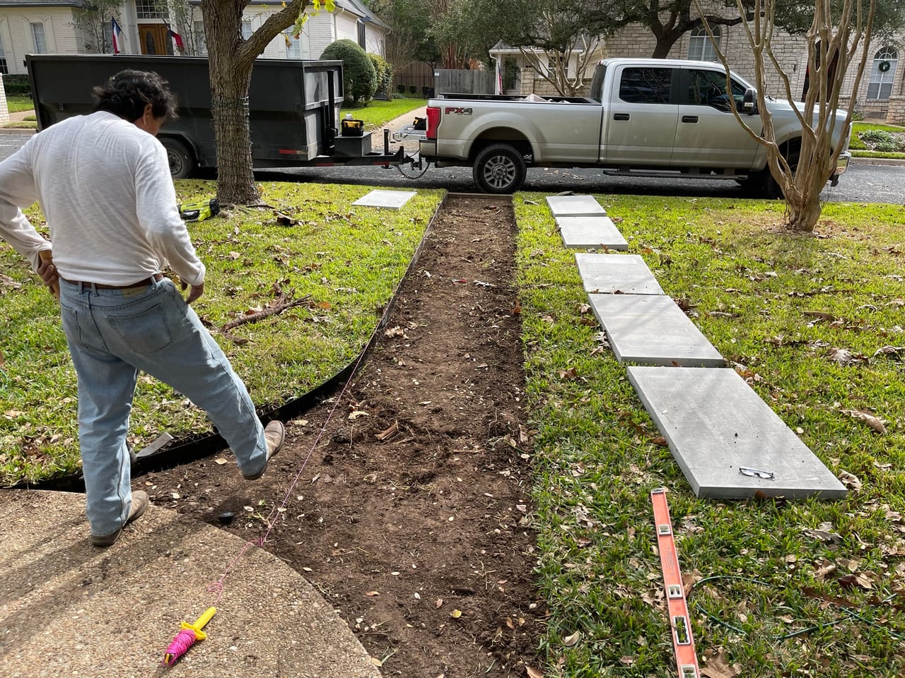 Worker setting concrete paver steppers across a front lawn trench by Corral Bros in Central Texas