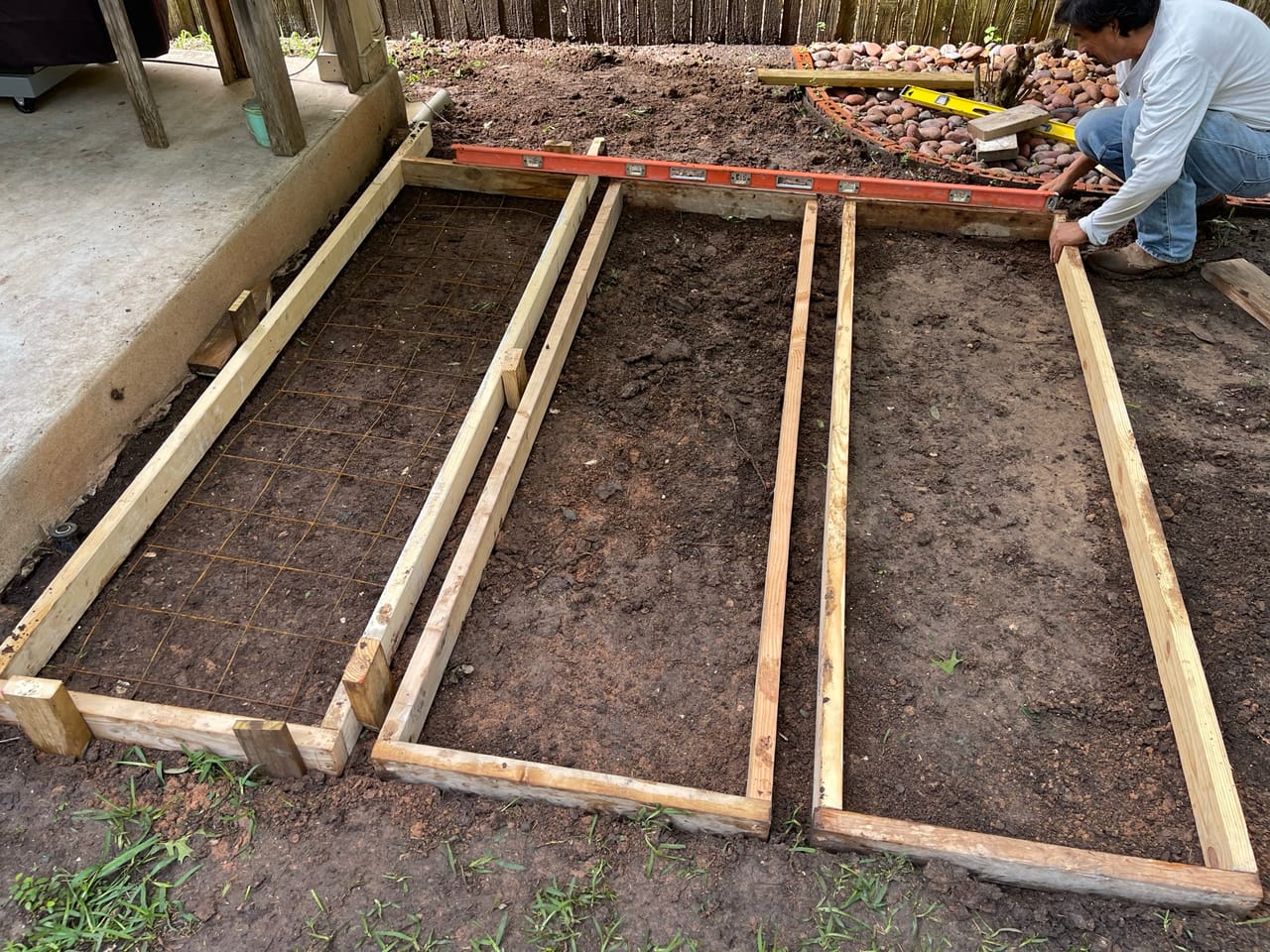 Worker setting wood forms for a concrete walkway over bare dirt by Corral Bros in Central Texas