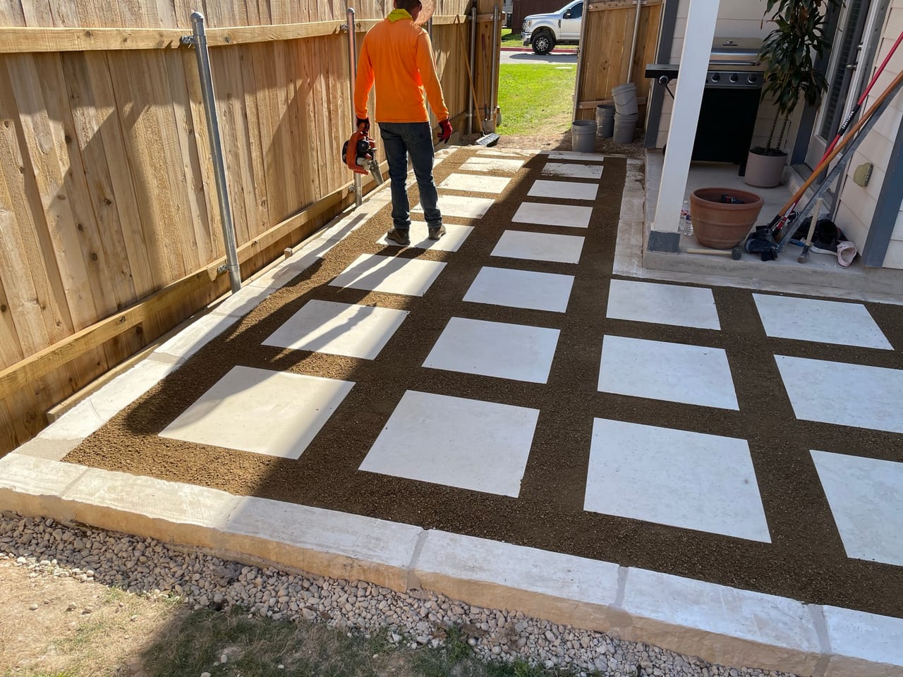 Worker walking a finished checkerboard paver walkway between fence and house in Georgetown, TX