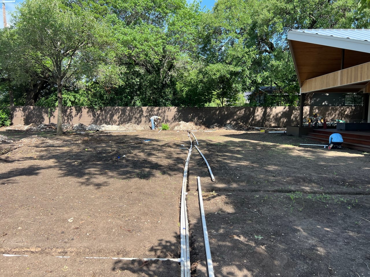 Irrigation lines stretched across a bare dirt yard under trees in Round Rock, TX