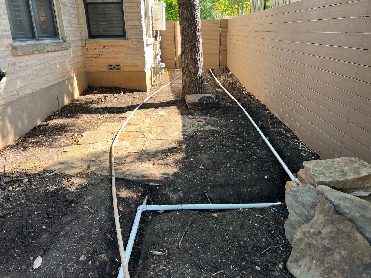 PVC irrigation lines routed between the house and a fence in Kyle, TX