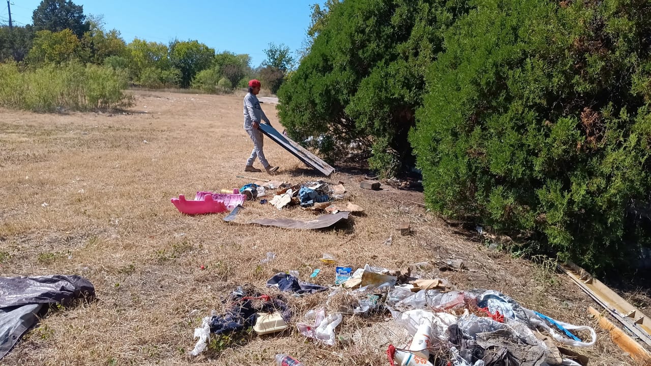 Crew member dragging a debris tarp across a trash littered lot in Central Texas
