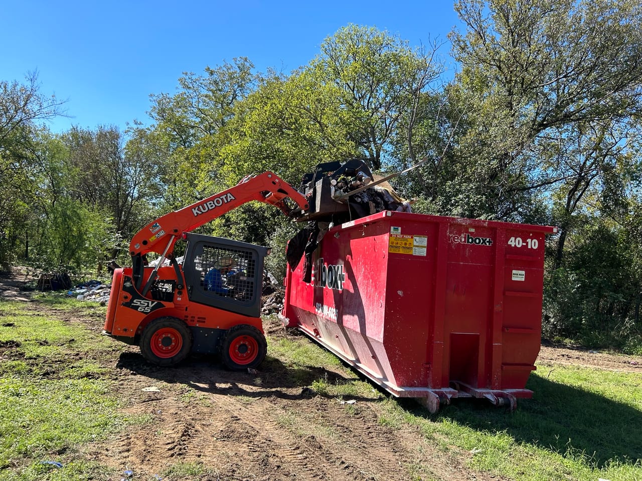 Red Kubota skid steer loading debris into a roll off dumpster in Round Rock, TX