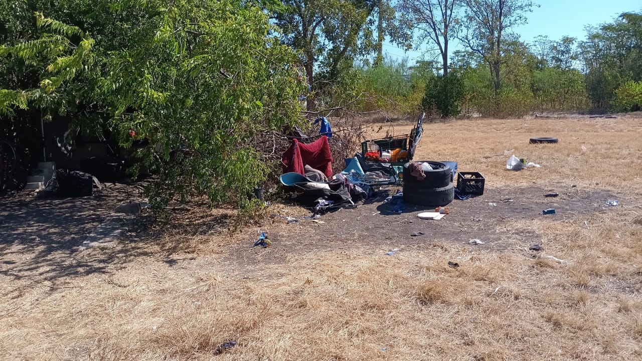 Scattered trash and abandoned belongings spread across a dry lot in Lockhart, TX