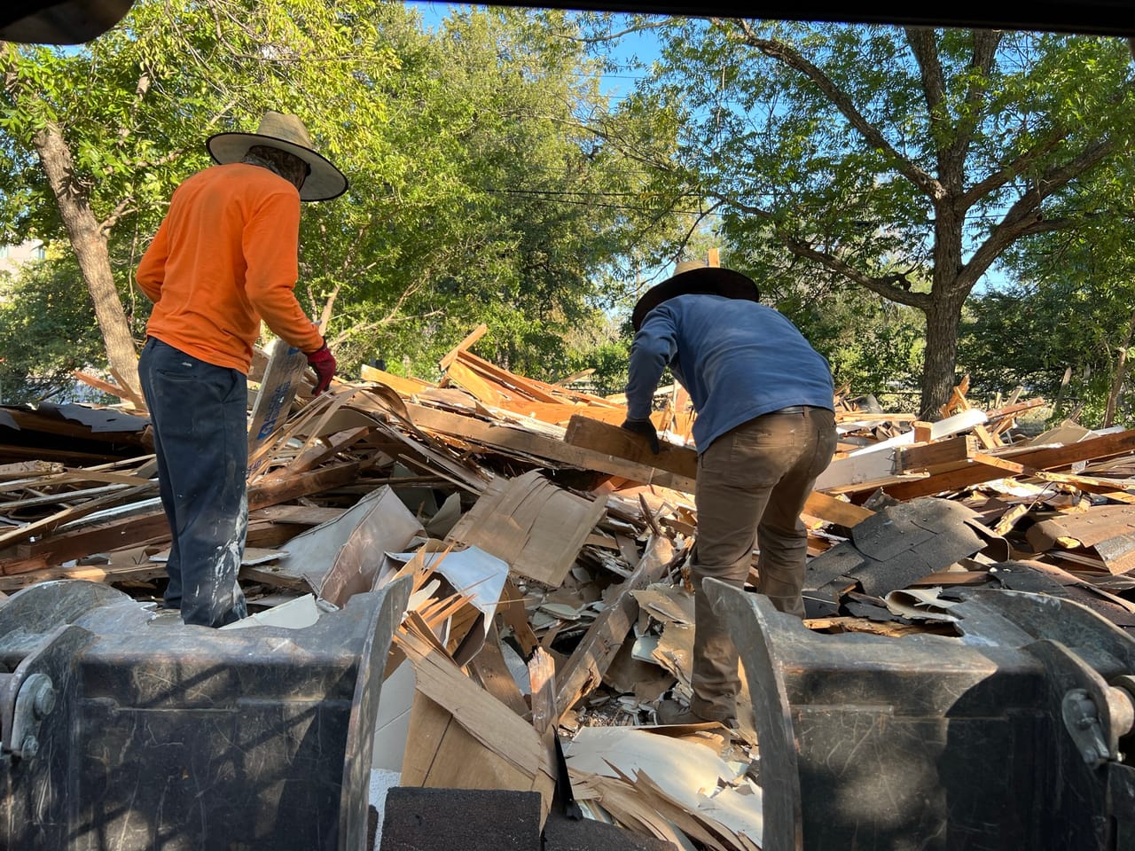 Two workers standing atop a heaped wood debris load in a trailer in Georgetown, TX