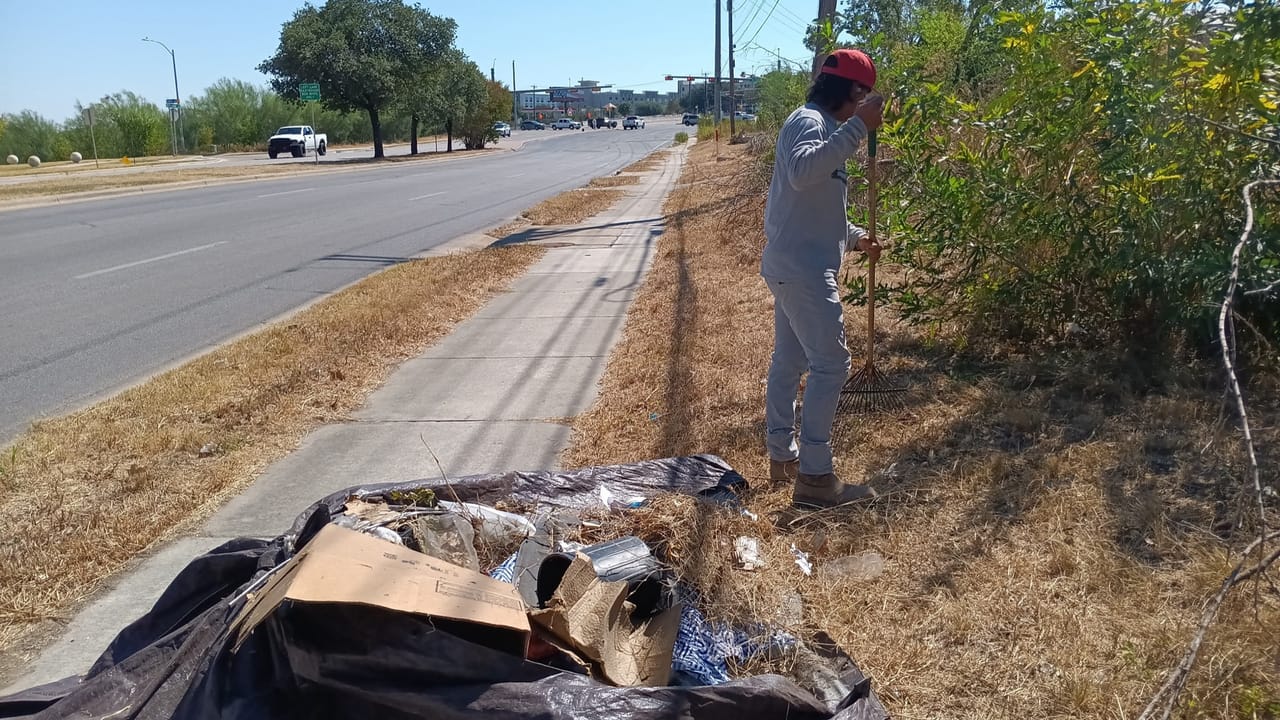 Worker gathering roadside debris onto a tarp along a rural street shoulder in Georgetown, TX