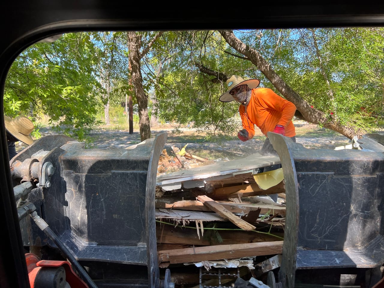 Worker loading torn lumber into a dump trailer, shot through a window in Dripping Springs, TX