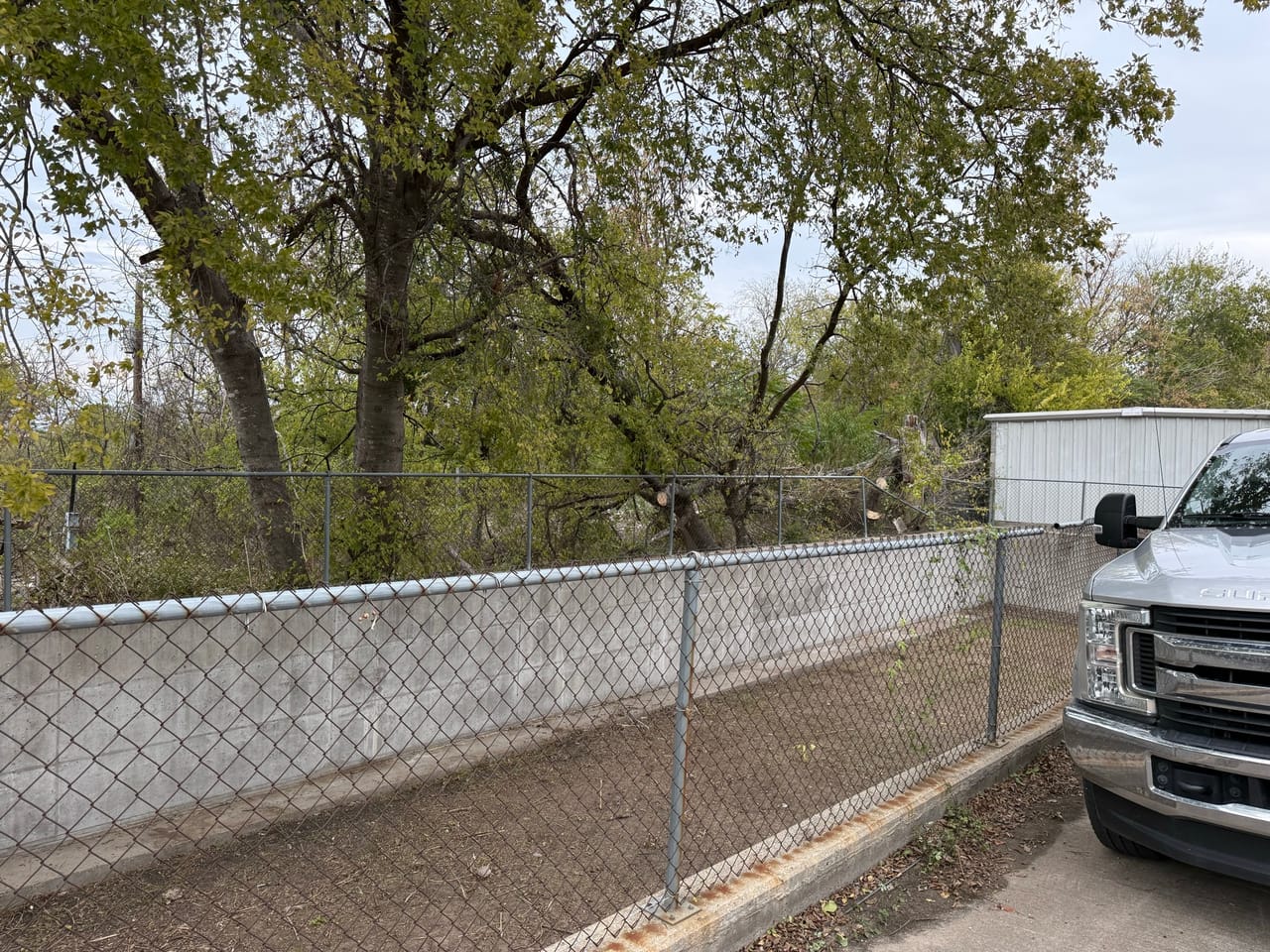 Cleared fence line and work truck parked along a dirt shoulder in Bastrop, TX