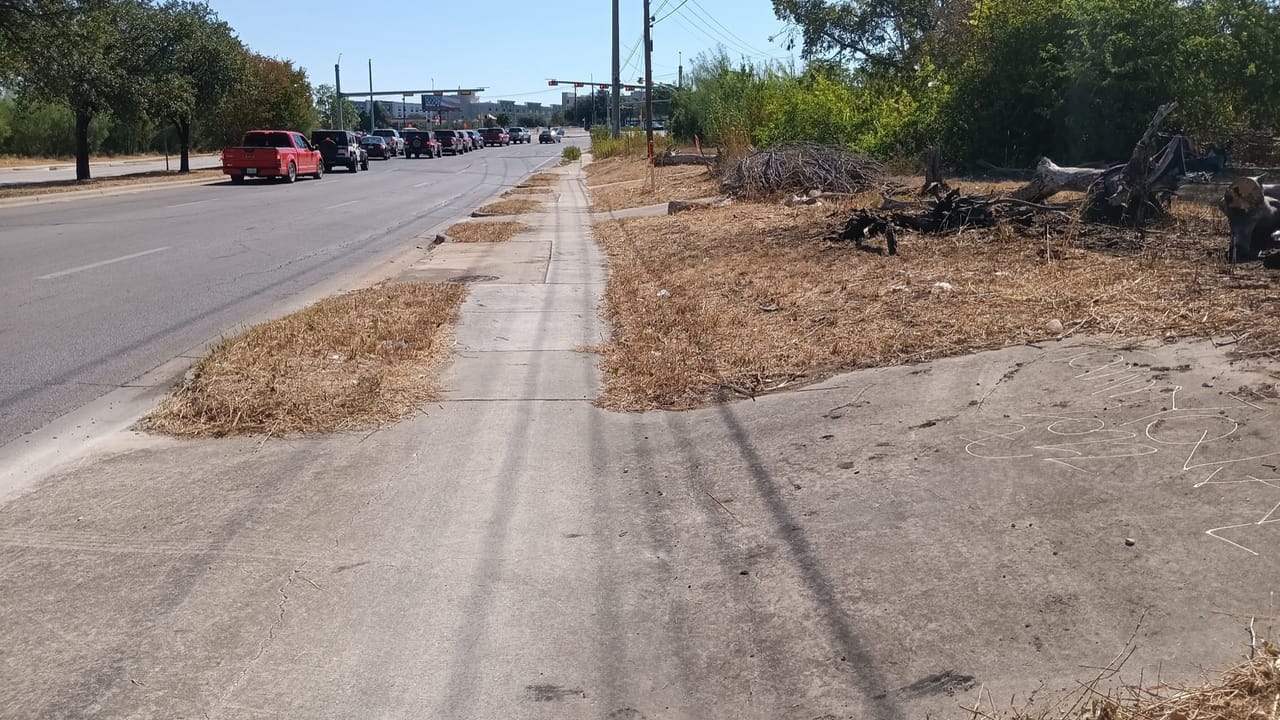 Cleared roadside strip and sidewalk with brush debris beside parked cars in Leander, TX