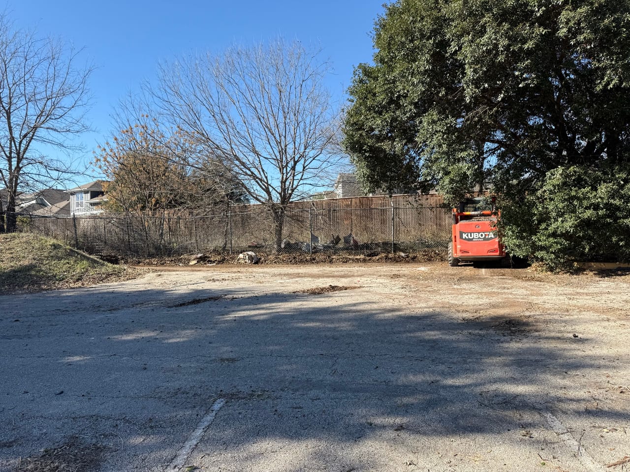 Cleared vacant lot with a small skid steer parked near the treeline in Central Texas