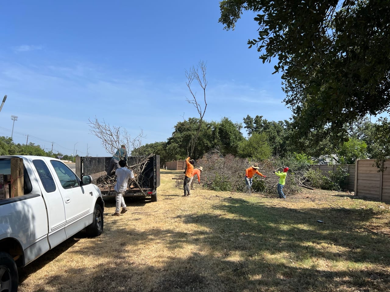 Crew loading brush into a dump trailer behind a white pickup in Cibolo, TX