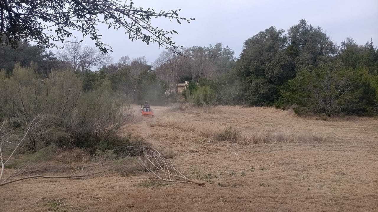 Dust cloud from brush mowing across a wide overgrown winter field in Central Texas