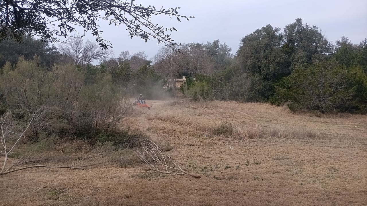 Dust rising from brush mowing across a wide overgrown dry field in Leander, TX
