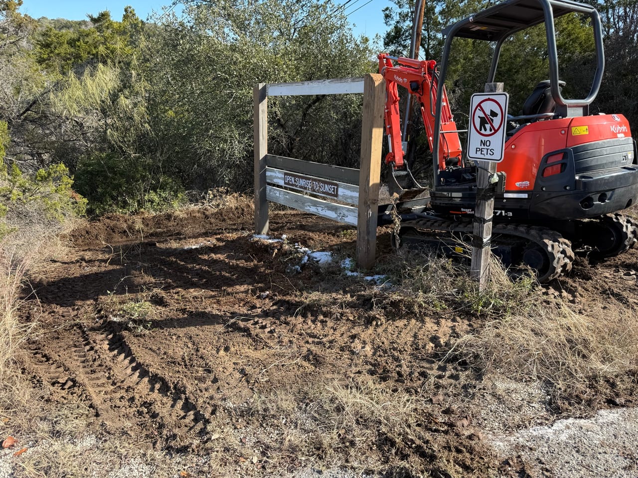 Mini excavator parked by a metal gate on freshly cleared ground in Elgin, TX