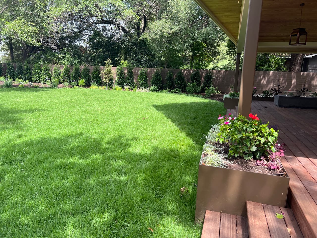 Backyard lawn seen from a covered patio with flower planter in Round Rock, TX