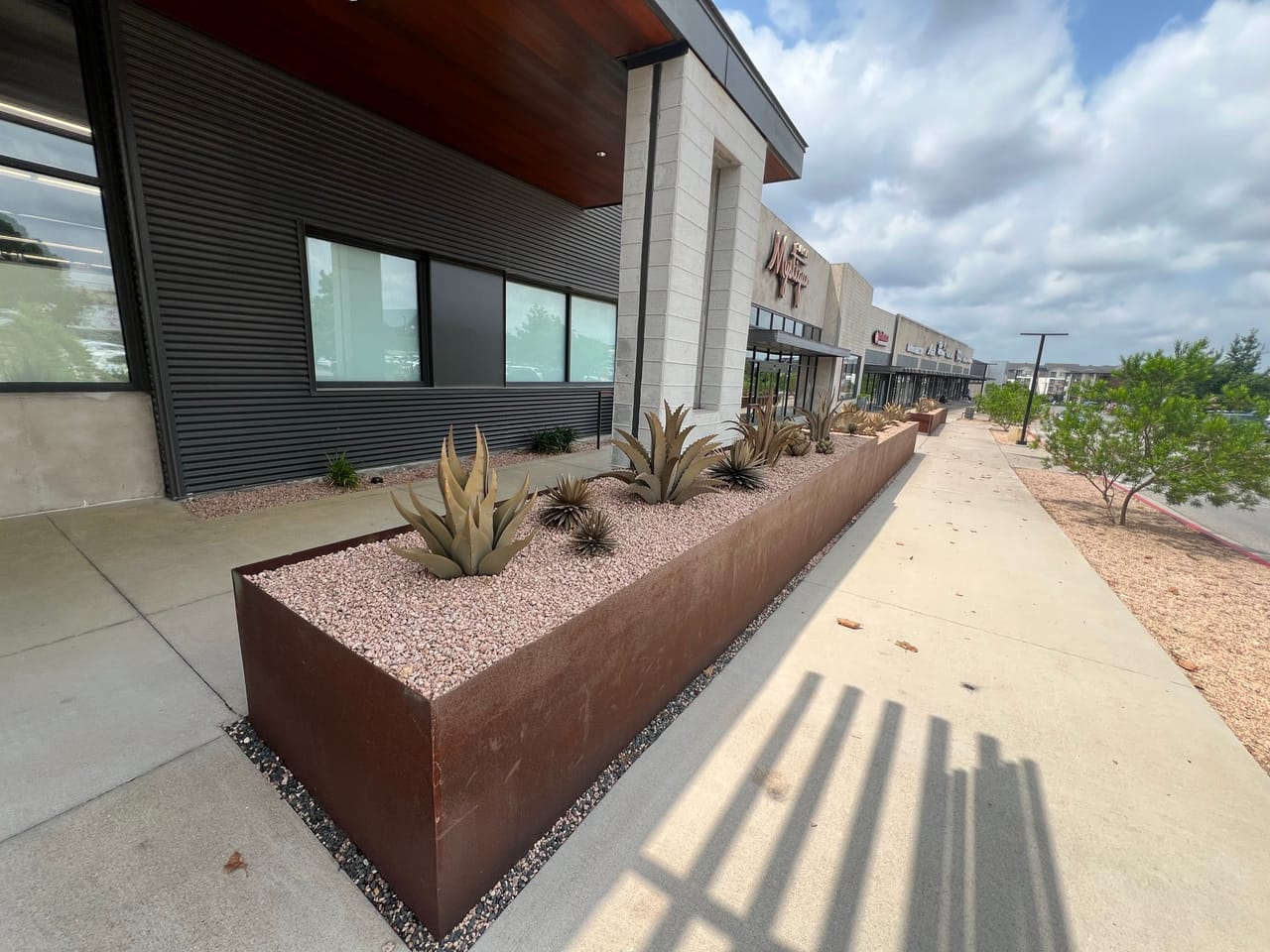 Corten steel planter with gravel and metal agave sculptures at retail center in Leander, TX