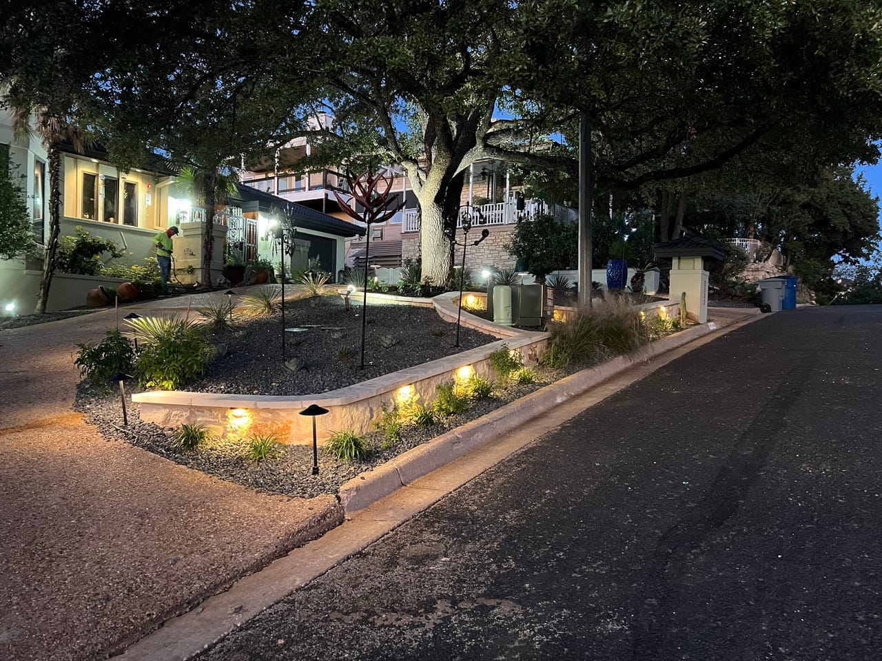 Lit planting beds and low stone curb along a driveway at dusk in Central Texas