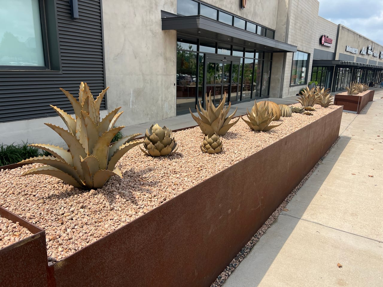 Retail center planter with agave and artichoke sculptures in gravel in Pflugerville, TX