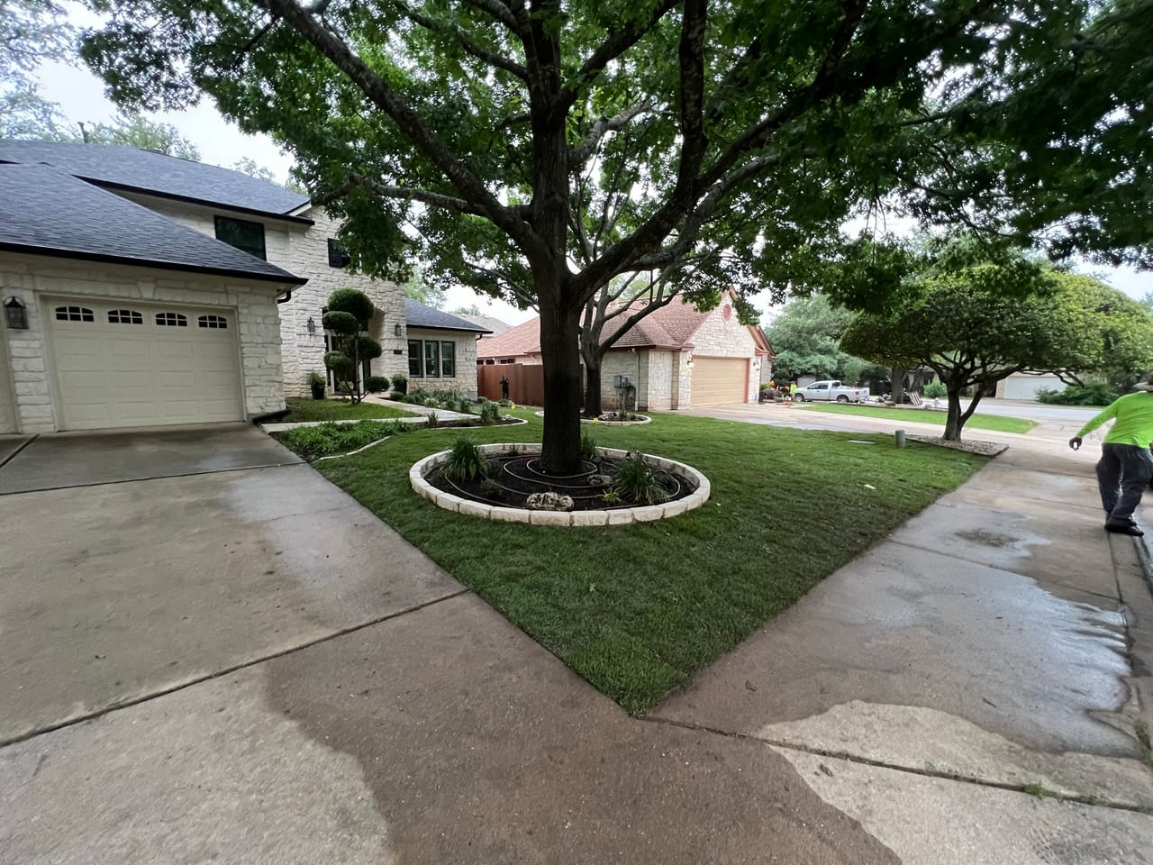 Stone edged tree ring and crisp green lawn in front of brick home in Kyle, TX