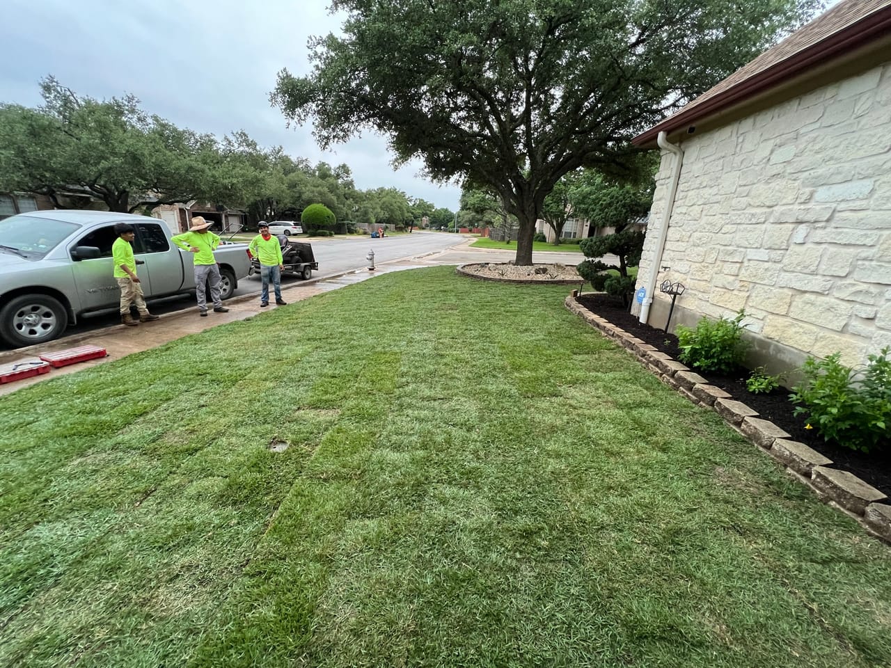 Manicured front lawn with crew and work truck at the curb in Kyle, TX