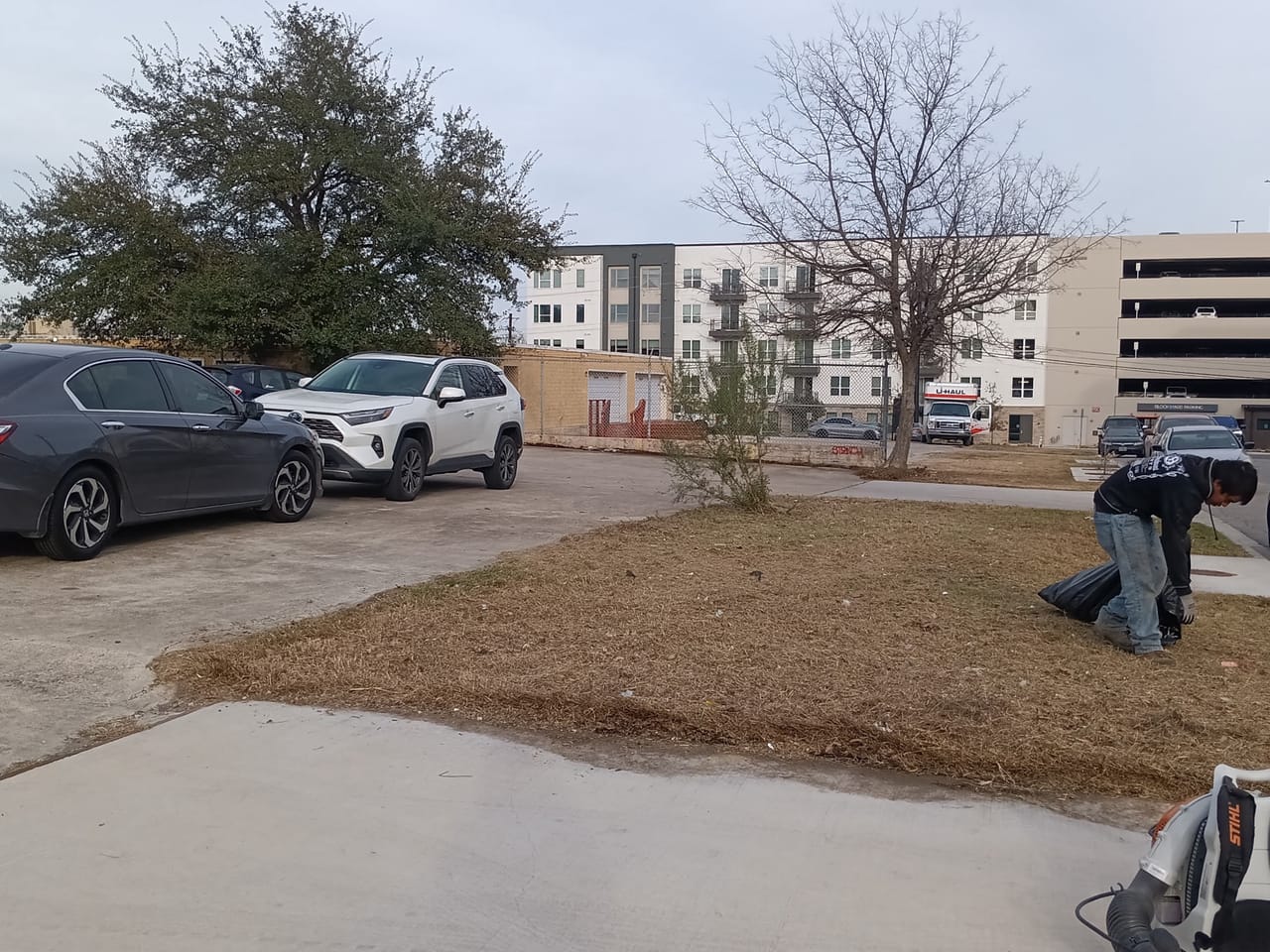 Worker running a backpack blower on dormant lawn at apartment complex in Leander, TX