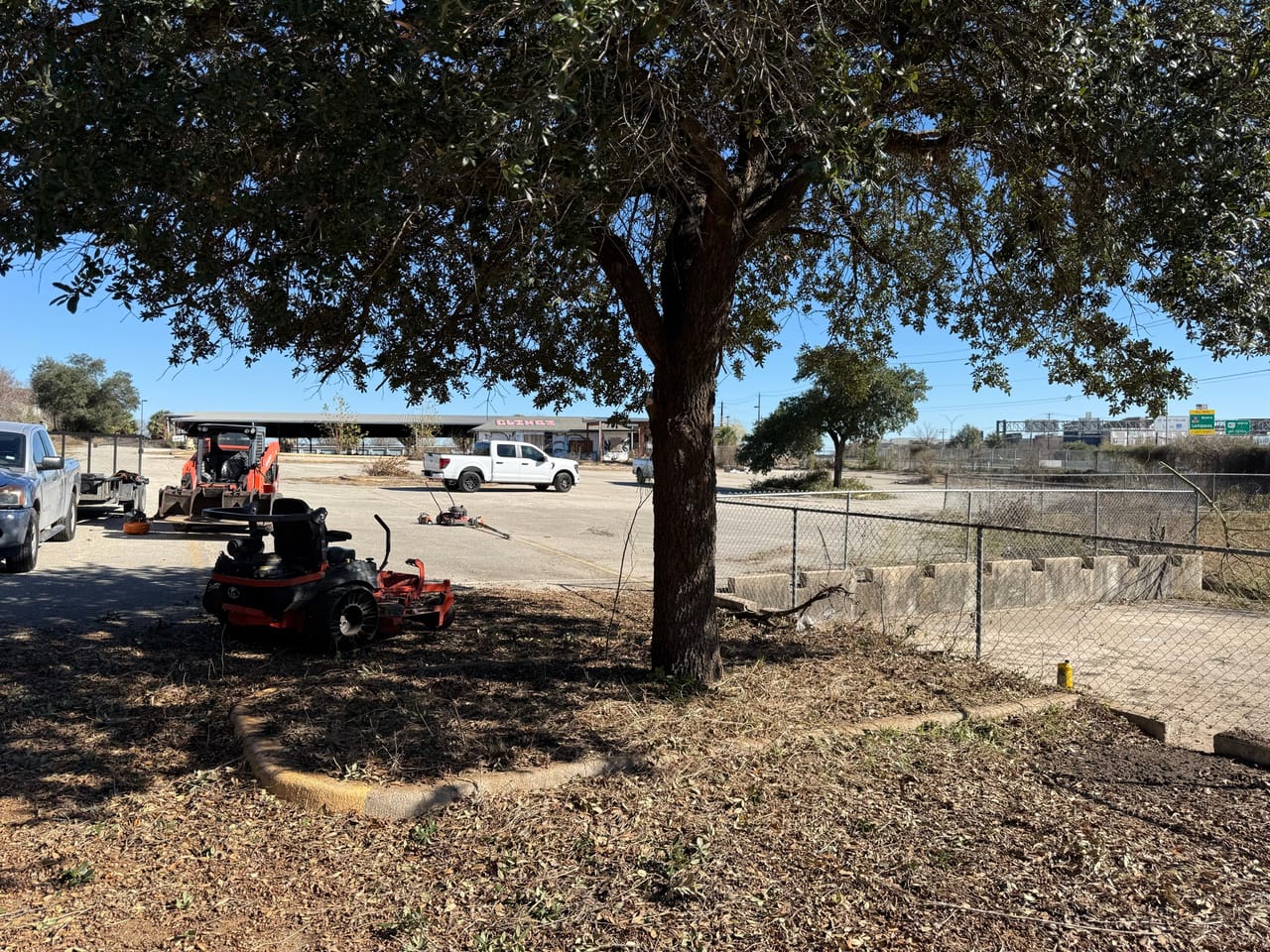 Zero turn mower working under a live oak with crew trucks nearby in Kyle, TX