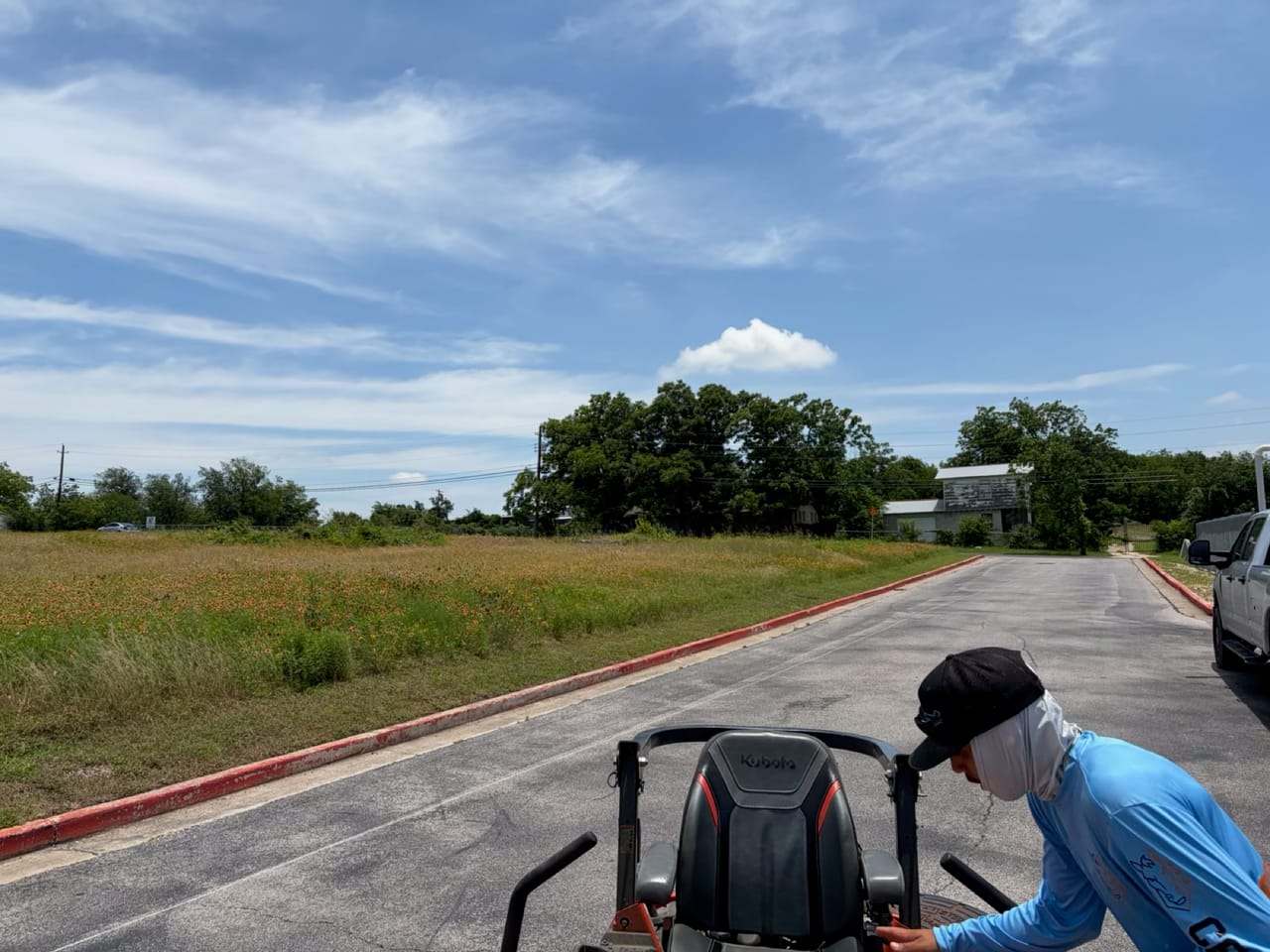 Operator riding a mower along a curbed lot on a sunny day in Round Rock, TX
