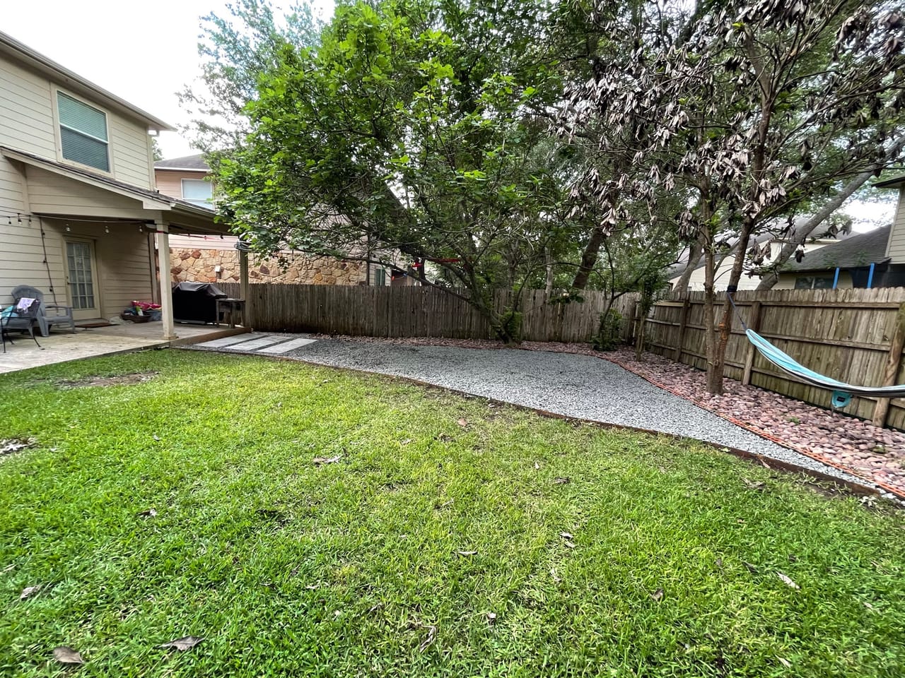 Backyard lawn with new gravel bed and edging along wood fence in Pflugerville, TX