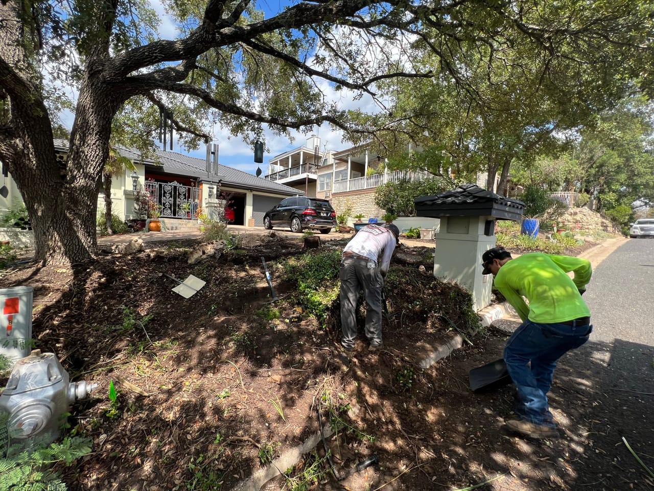 Crew spreading dark mulch in a street median bed under oaks by Corral Bros in Central Texas