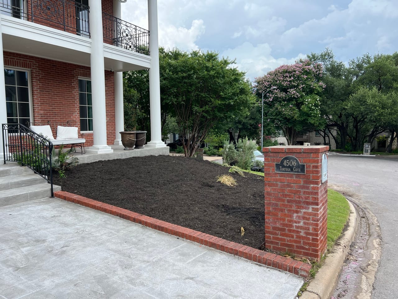 Fresh black mulch bed beside a brick walkway and columned porch in Georgetown, TX