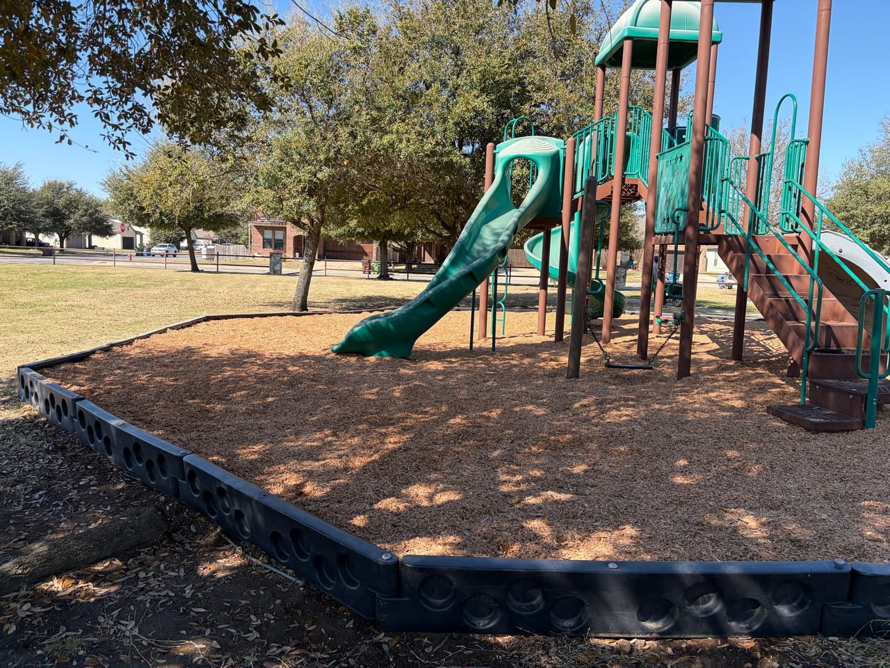 Fresh brown mulch spread evenly around green playground equipment in Pflugerville, TX