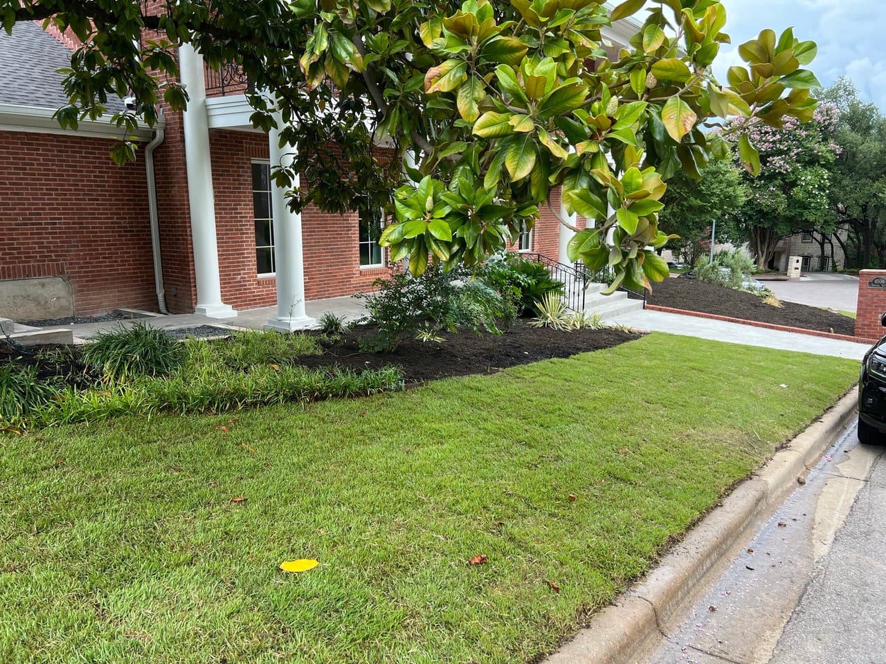 Fresh dark mulch bed and green lawn along a brick building in Round Rock, TX